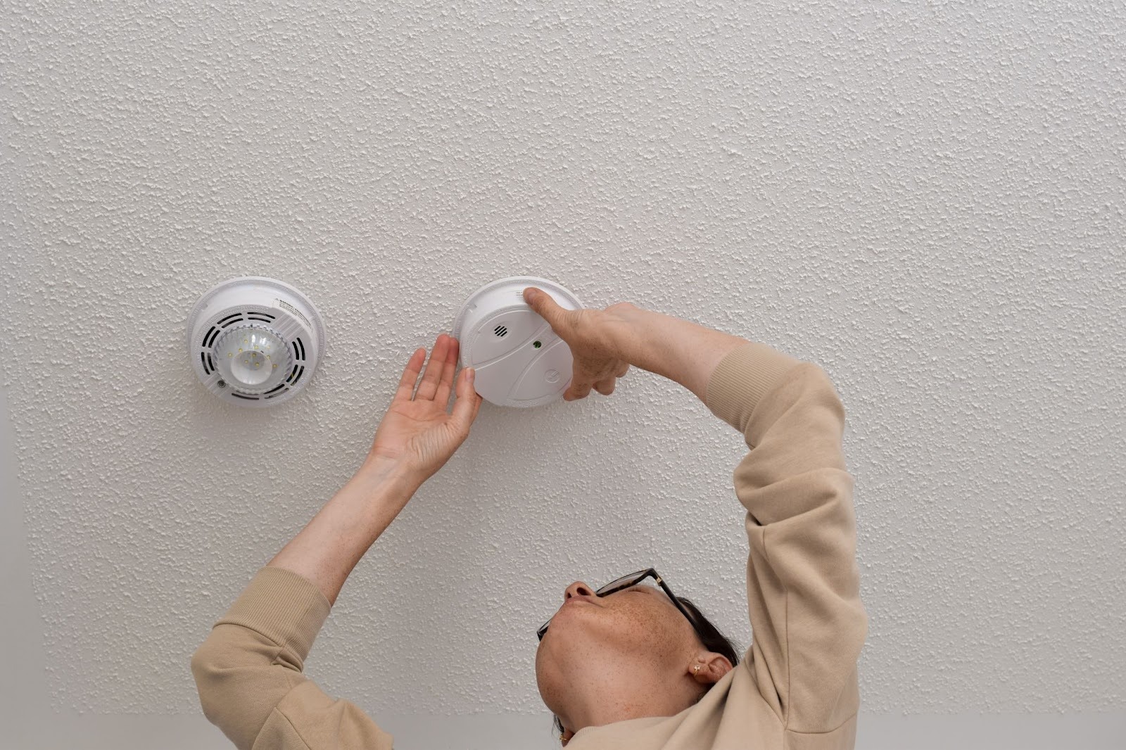 Alt-text: A technician’s hand mounting a carbon monoxide detector on a ceiling.