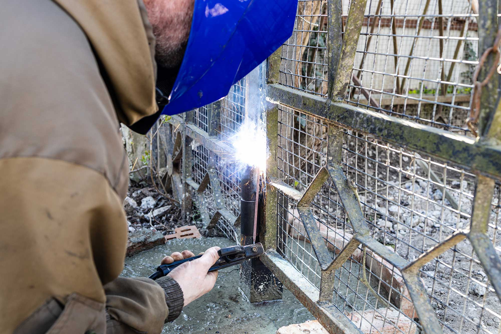 A welder in protective gear repairs a metal structure, with bright sparks flying from the welding torch. The scene emphasizes the urgency and skill involved in emergency welding repairs.
